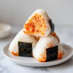 A stack of three triangular tuna rice balls (onigiri) wrapped partially with nori seaweed, showing the orange tuna filling.