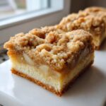 A close-up of a thick, square portion of apple crumb bars showing the bottom crust, apple filling, and crumb topping.