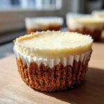 A single, perfectly baked cheesecake cupcake with a thick graham cracker crust, sitting on a wooden surface.