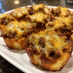 Close-up of baked hanky panky recipe appetizers served on a white platter, featuring browned bread cups topped with savory meat mixture and melted cheese.