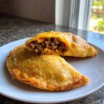Two golden-brown cheesy pocket tacos on a white plate, one cut open showing seasoned ground beef and melted cheese.