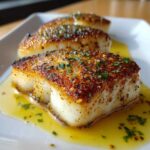 Close-up of three perfectly seared portions of chilean sea bass recipe resting in a pool of lemon butter sauce.