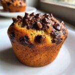 Close-up of a golden brown chocolate chip muffins recipe, topped generously with melted chocolate chips.