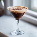 A decadent chocolate martini served in a coupe glass, topped with creamy foam and chocolate shavings.