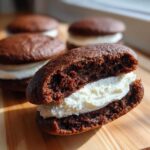 A close-up cross-section view of a chocolate whoopie pie showing the rich cake texture and thick white cream filling.
