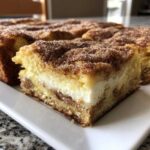 A thick square slice of churro cheesecake bars showing layers of cake, cream cheese filling, and cinnamon sugar topping.