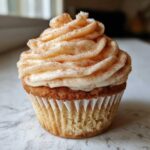 A close-up of a single, delicious churro cupcake topped with swirled cinnamon frosting.