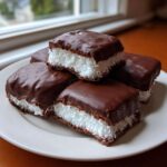 A stack of homemade cool whip candy bars featuring a white coconut filling sandwiched between chocolate cake layers and coated in rich chocolate.