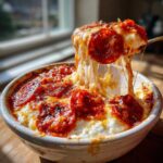 A spoonful of cheesy cottage cheese pizza bowl being lifted, showing a dramatic cheese pull with pepperoni slices.