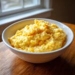 A close-up shot of a white bowl filled with creamy cheese grits, featuring melted orange cheddar.
