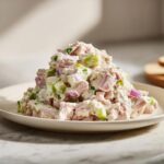 A mound of creamy ham salad featuring diced ham, celery, and red onion served on a light plate.