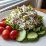 A mound of creamy chicken salad served over lettuce, garnished with cherry tomatoes and cucumber slices, a perfect high protein salad.