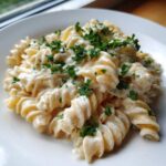Close-up of creamy protein pasta (fusilli) coated in a white sauce and topped with fresh chopped parsley.