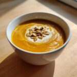 A close-up of creamy pumpkin soup topped with a swirl of cream and toasted pumpkin seeds.