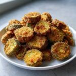 A white plate piled high with golden brown, crispy slices from a fried okra recipe.