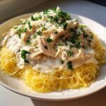 A bowl of angel hair pasta topped with creamy crock pot angel chicken and fresh parsley.