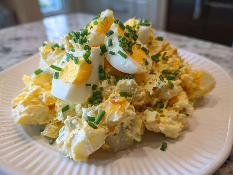 A mound of creamy deviled egg potato salad topped with sliced hard-boiled eggs and fresh chives.