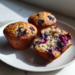 Three fluffy cottage cheese blueberry muffins, one broken open to show the moist interior filled with blueberries.