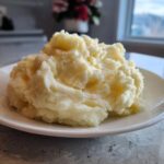 A generous serving of fluffy, creamy mashed potatoes piled high on a white plate.