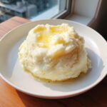 A generous serving of fluffy mashed potatoes recipe topped with melting butter in a white bowl.