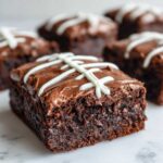 A fudgy, square football brownie topped with chocolate frosting and white icing laces, sitting on a marble surface.