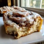 Close-up of a gooey cinnamon roll covered in thick white icing, showing the soft dough texture.