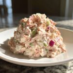 A mound of creamy ham salad recipe featuring shredded ham, celery, and red onion on a white plate.