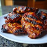 Close-up of several pieces of glazed and grilled hawaiian huli huli chicken stacked on a white plate.