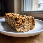 Close-up of a thick, homemade chocolate chip protein bar made with oats, resting on a white plate.