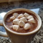 Close-up of steaming homemade hot cocoa topped with fluffy white marshmallows in a white mug.