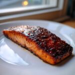 Close-up of a perfectly cooked salmon fillet glazed with a dark, sticky honey garlic butter sauce.