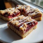 Four squares of homemade cherry pie bars with a crumb topping and white icing drizzle, sitting on a white plate.