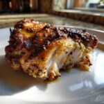 Close-up of a perfectly cooked, juicy piece of seasoned chicken thighs with a crispy, dark crust.