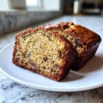 Two moist slices of greek yogurt banana bread with visible chocolate chips on a white plate.