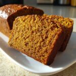 Close-up of moist, dark orange slices of easy pumpkin bread displayed on a white plate.