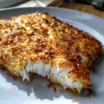 Close-up of two flaky white fish fillets with a perfectly golden, crispy parmesan crusted tilapia topping.
