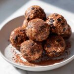 A pile of rich peanut butter protein balls studded with chocolate chips and dusted with cocoa powder.