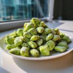 A mound of bright green pistachio puppy chow coated in powdered sugar sits on a white plate near a window.