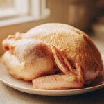 A raw, whole turkey resting on a white plate, ready for the turkey brine process.