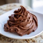 A beautiful swirl of rich, dark chocolate buttercream frosting piped onto a small white plate.