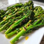 Close-up of bright green roasted broccolini stalks seasoned with garlic and oil on a white plate.
