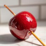 Close-up of a perfectly glazed, bright red candy apple on a wooden stick, ready to eat.