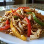 Close-up of shredded chicken mixed with colorful bell peppers and onions for crockpot chicken fajitas.
