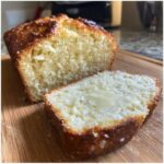 A slice of freshly baked beer bread, topped with melting butter, next to the rest of the loaf.