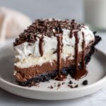 A decadent slice of Mississippi Mud Pie featuring layers of chocolate, cream, and a dark crust, topped with whipped cream and chocolate syrup.