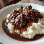 Close-up of shredded beef smothered in rich brown gravy served over creamy mashed potatoes, perfect for a slow cooker beef manhattan recipe.