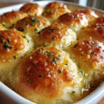 Close-up of golden brown, soft buttery rolls baked together and drenched in melted butter, topped with minced parsley.