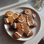 Three soft gingerbread cookies decorated with simple white icing smiles and buttons on a light plate.
