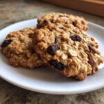 Close-up of three soft oatmeal raisin cookies stacked slightly on a white plate.