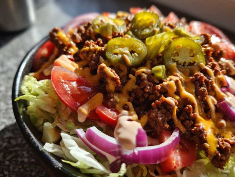 Close-up of a delicious cheeseburger bowl featuring seasoned ground beef, melted cheese, jalapeños, tomatoes, and red onion.